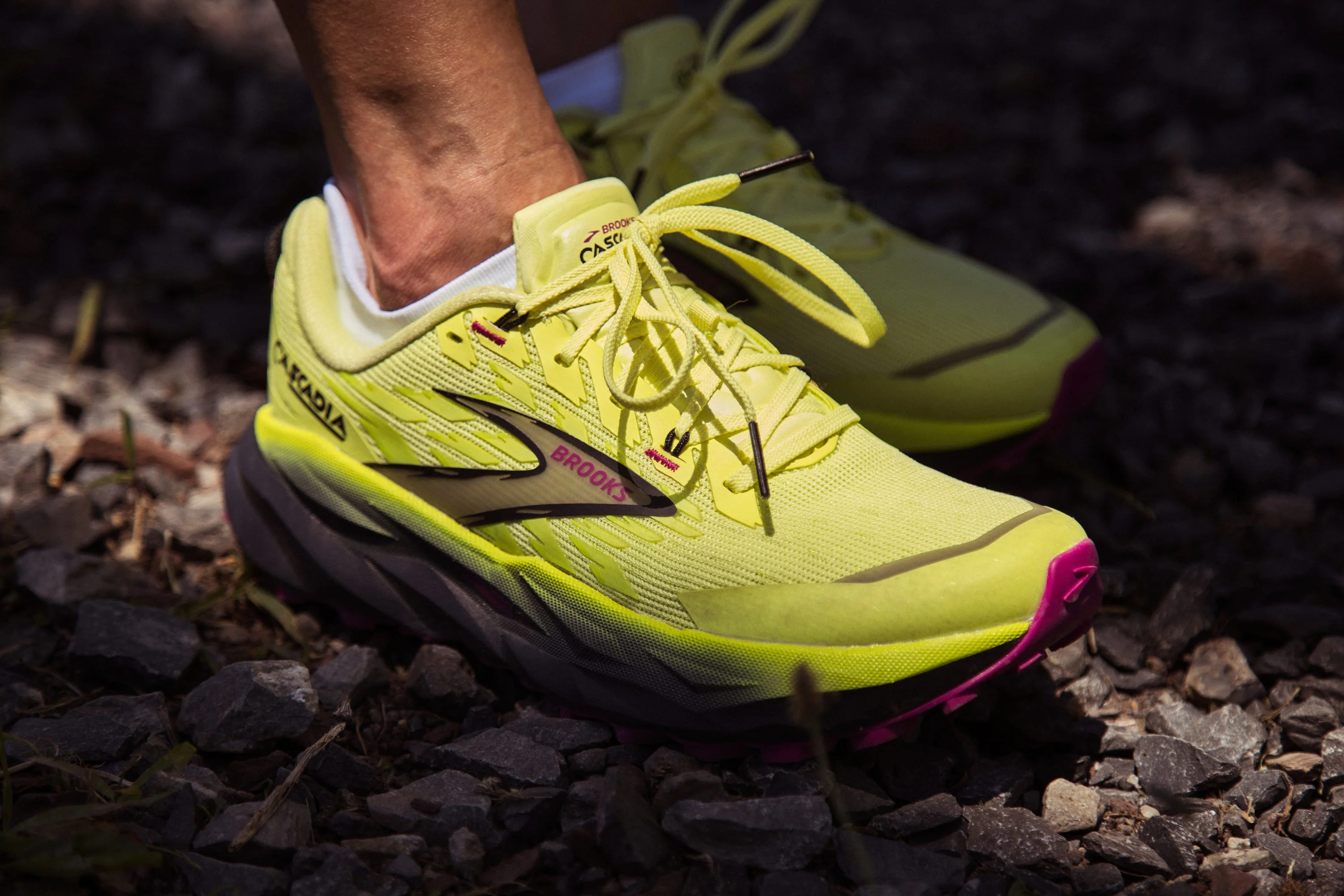 Yellow running shoes with pink accents on gravel.