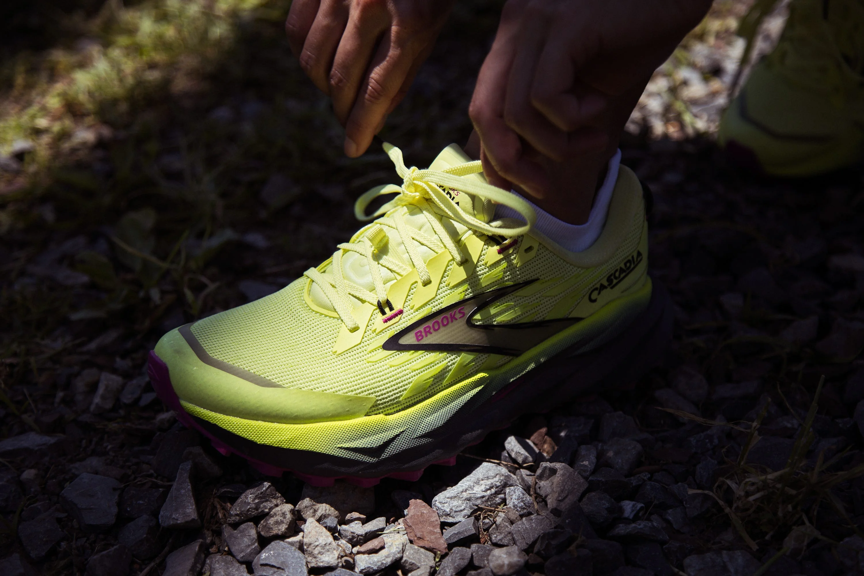 Person tying laces on a bright yellow Brooks running shoe on gravel.