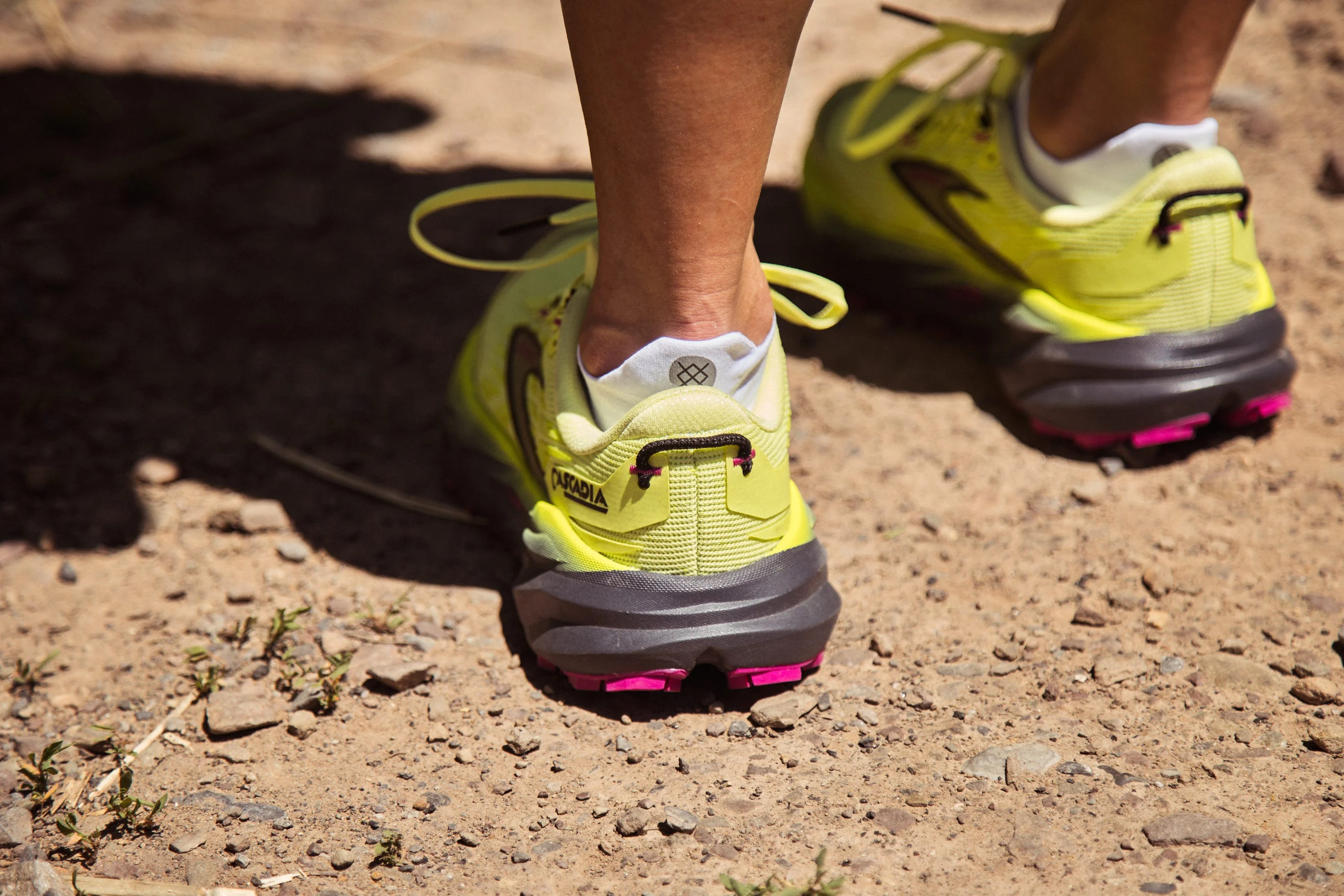 Runner wearing neon yellow trail shoes on a rocky path.