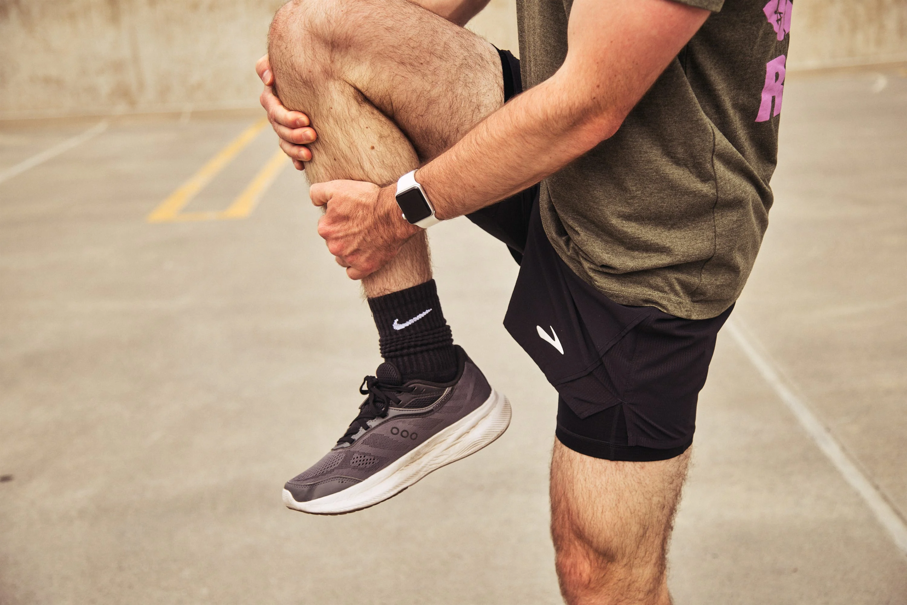 Runner stretching leg on a concrete surface wearing shorts and athletic shoes.