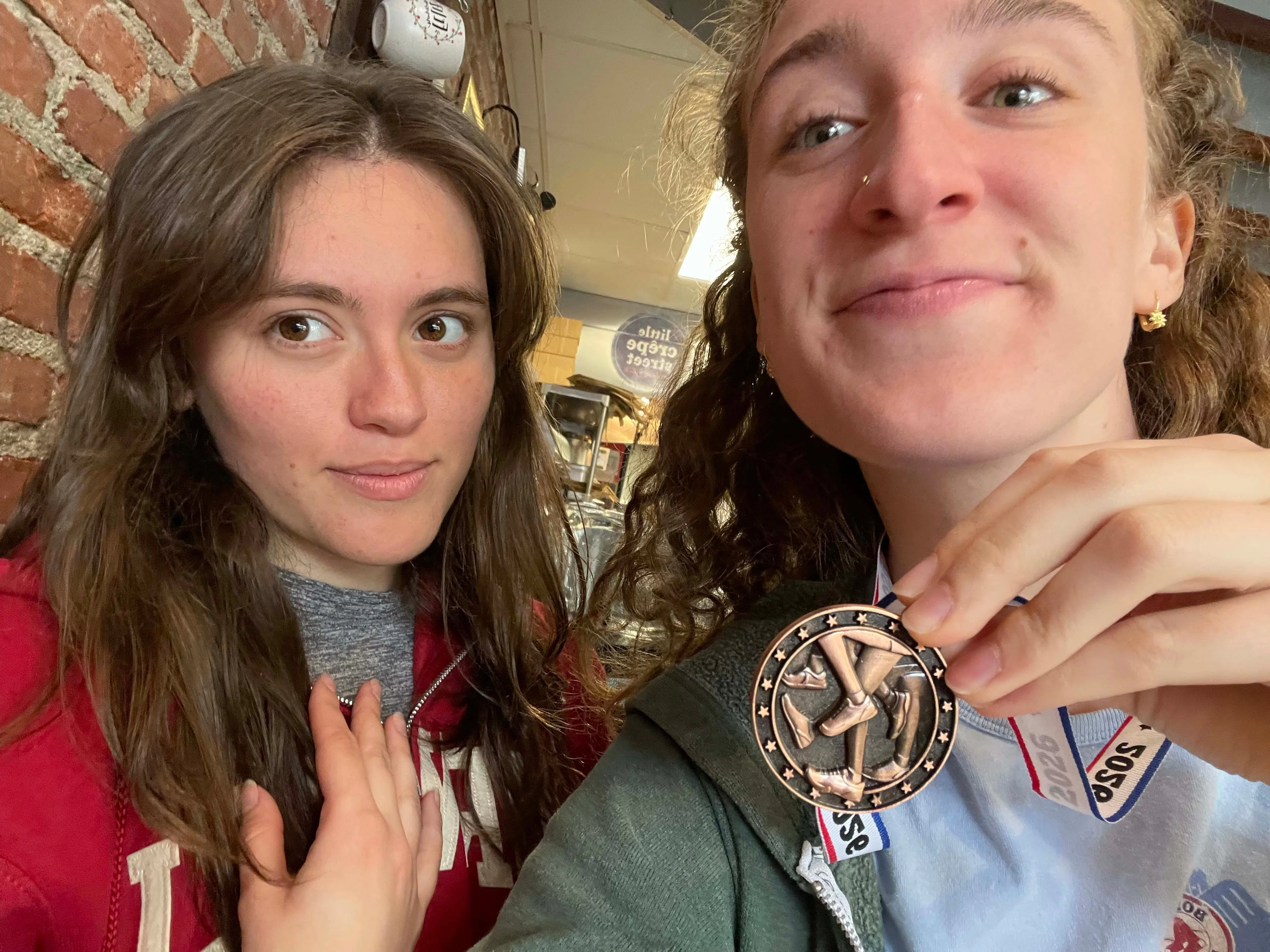 Two people smiling, one holding a medal in a cafe setting.