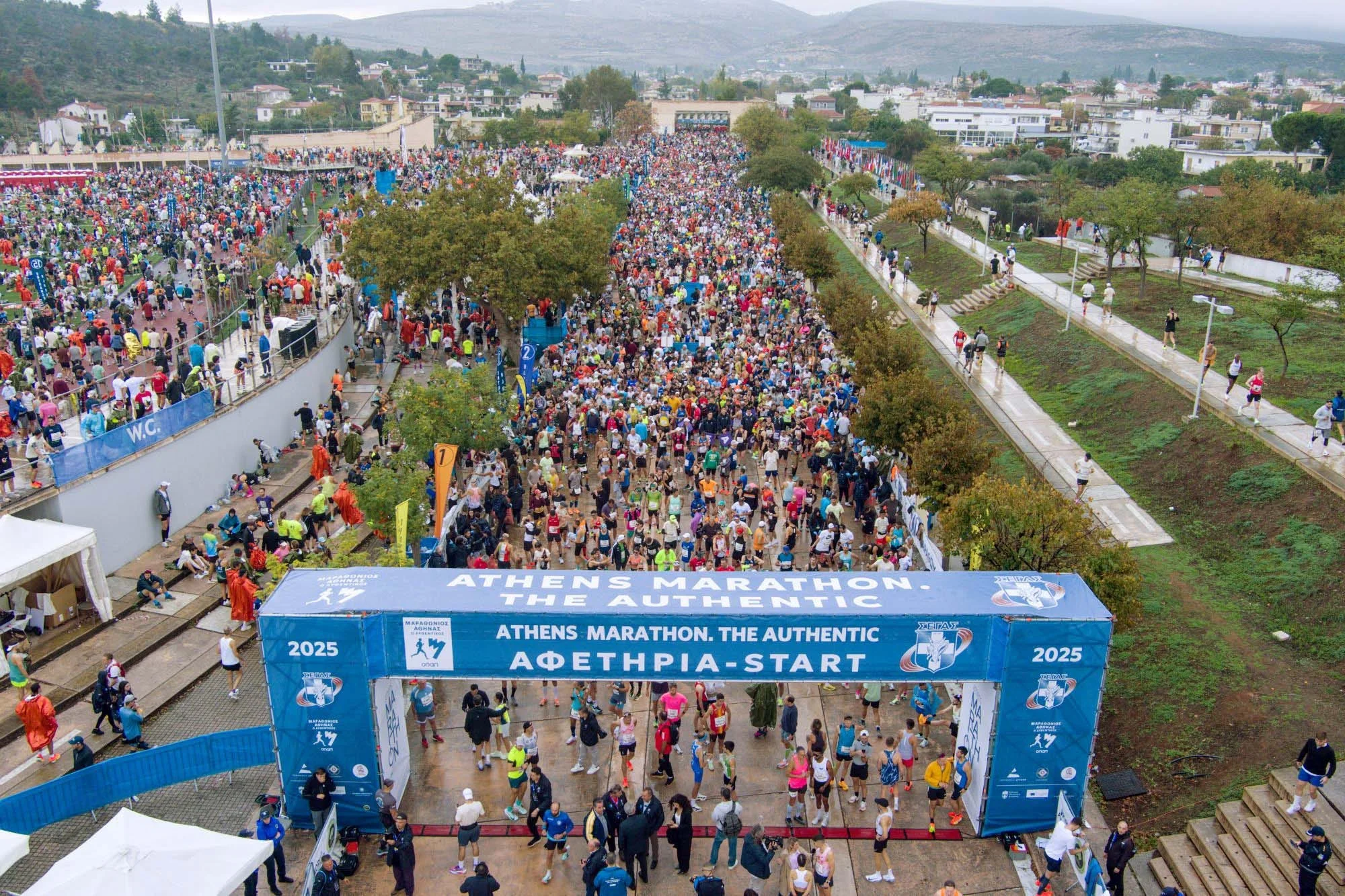 Crowd of participants gathering at the start of the Athens Marathon under a large blue archway. Crowd of participants gathering at the start of the Athens Marathon under a large blue archway.
