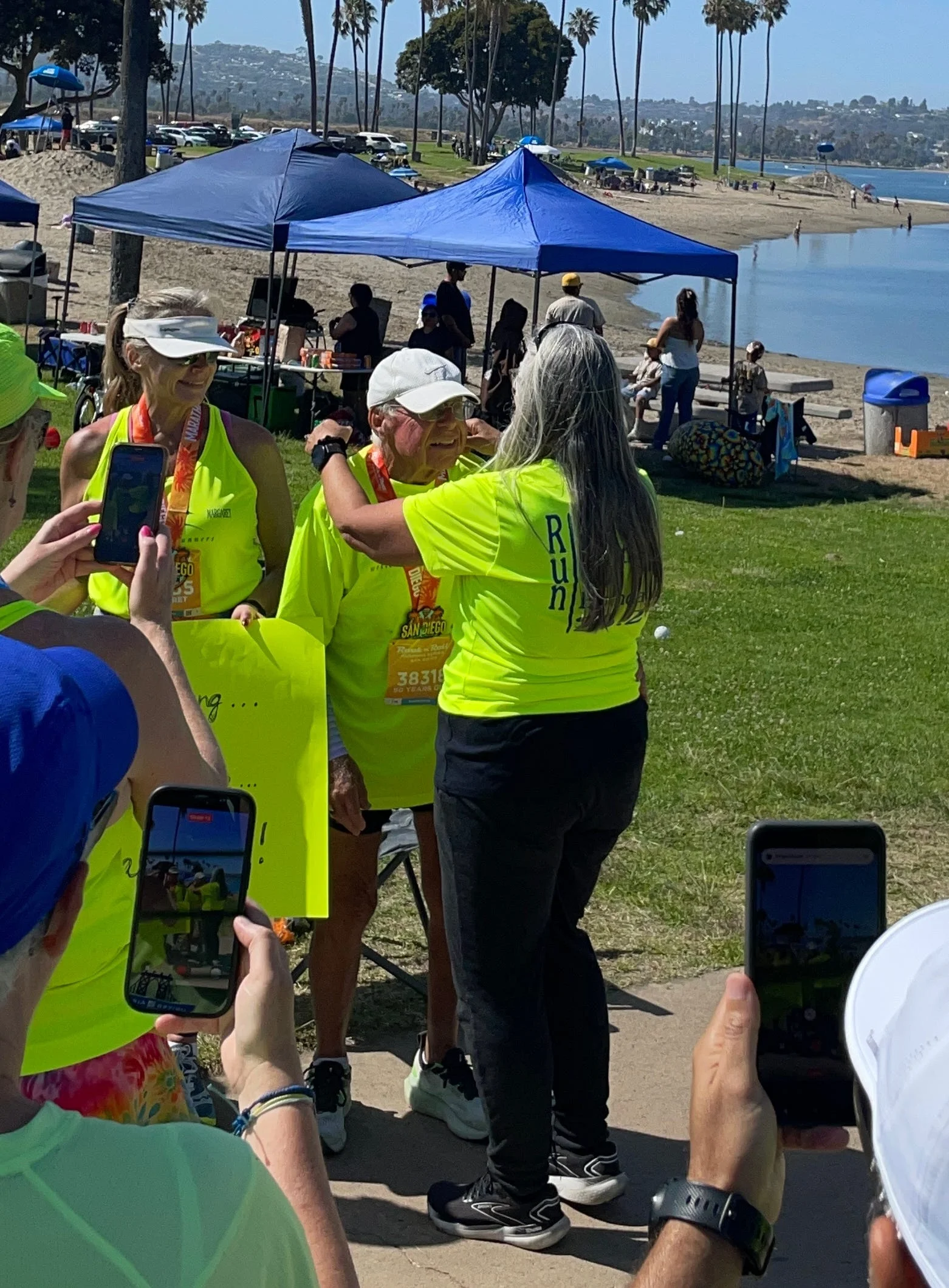 Runners in bright shirts celebrate at a beachside event, capturing memories with smartphones in sunny weather. Runners in bright shirts celebrate at a beachside event, capturing memories with smartphones in sunny weather.