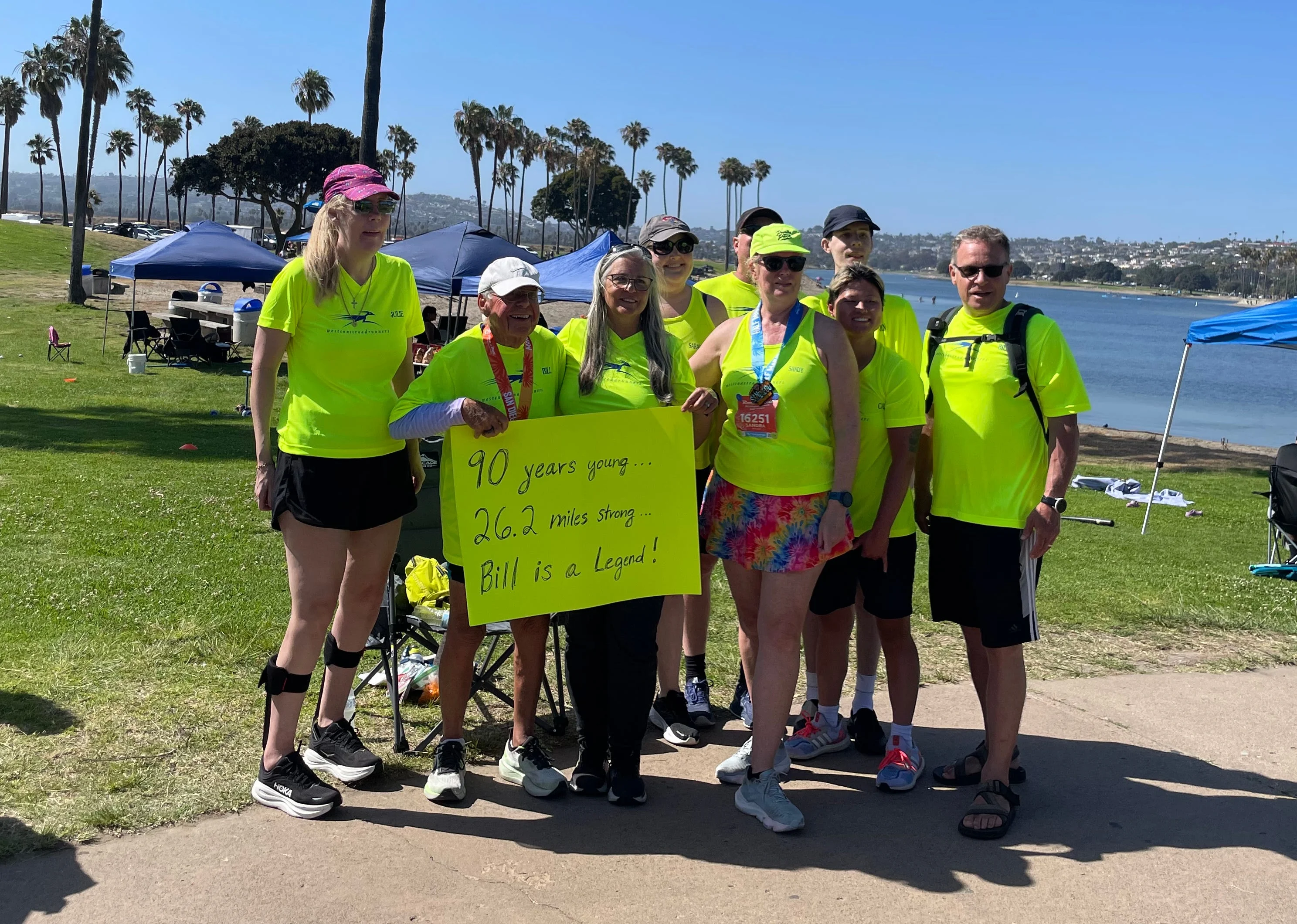 Group of runners celebrating a 90-year-old participant, holding a sign that recognizes his achievement. Group of runners celebrating a 90-year-old participant, holding a sign that recognizes his achievement.