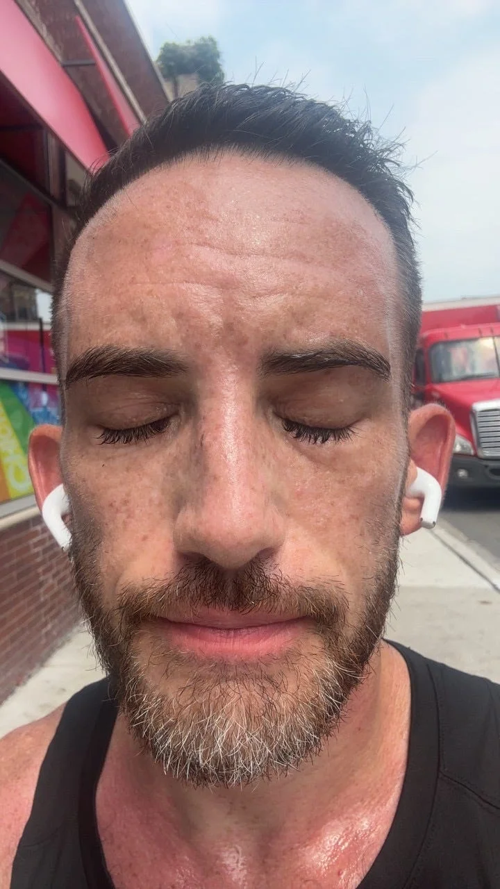 Man with closed eyes and earbuds, showing a focused expression, with a slightly sweaty face and a brick background. Man with closed eyes and earbuds, showing a focused expression, with a slightly sweaty face and a brick background.