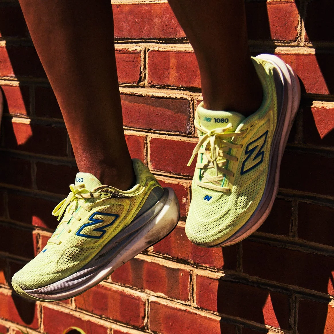 Close-up of vibrant yellow sneakers against a brick wall, with sunlight casting shadows during an active moment. Close-up of vibrant yellow sneakers against a brick wall, with sunlight casting shadows during an active moment.