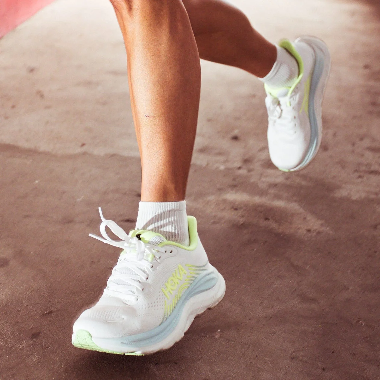 A person running in a green outfit and white sneakers on a concrete surface near a red wall. A person running in a green outfit and white sneakers on a concrete surface near a red wall.
