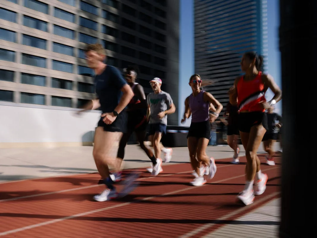 Group of runners training on an outdoor track with tall buildings in the background. Group of runners training on an outdoor track with tall buildings in the background.