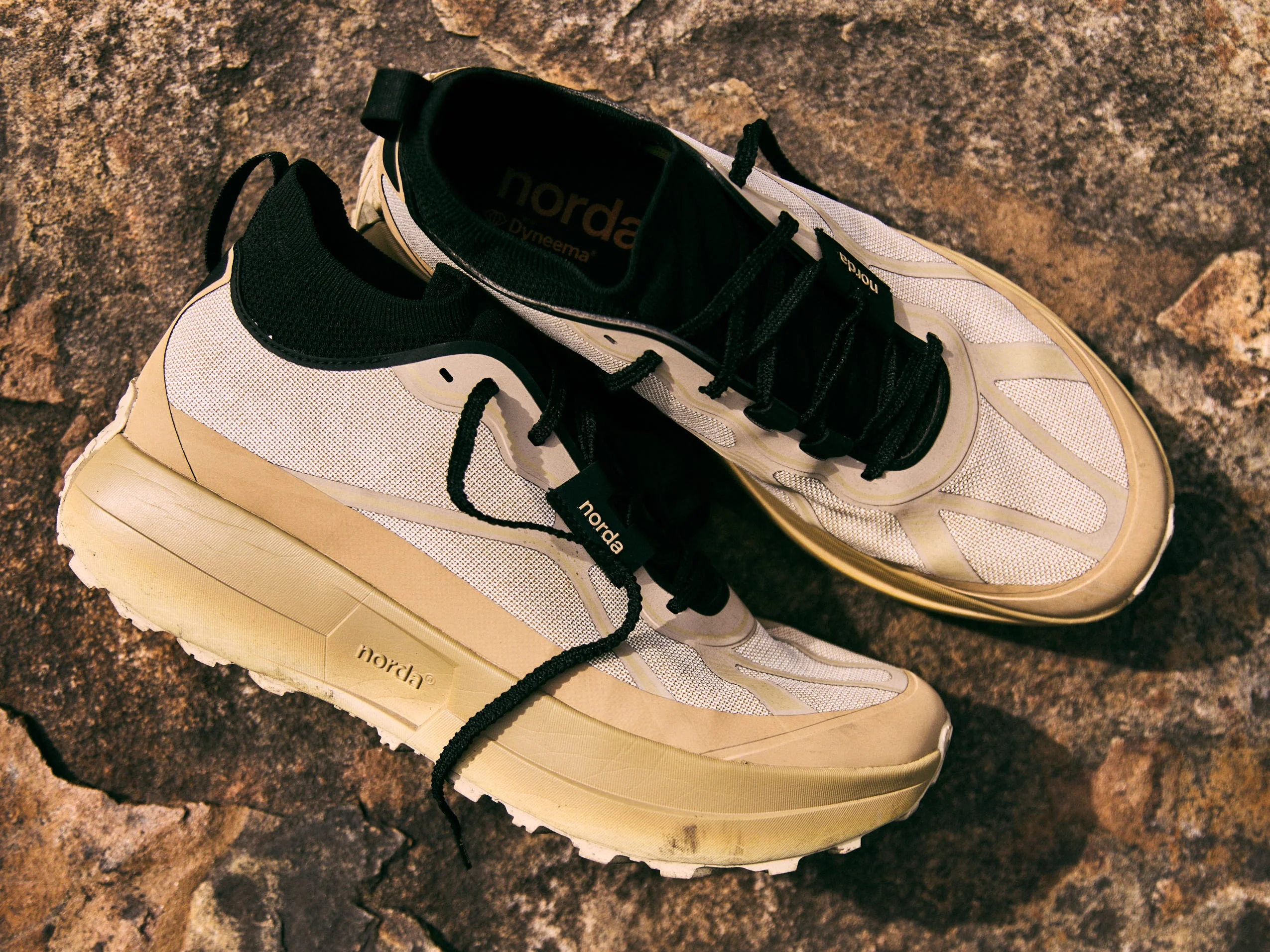Norda 055 running shoes with a beige and black design, resting on a rocky surface.
