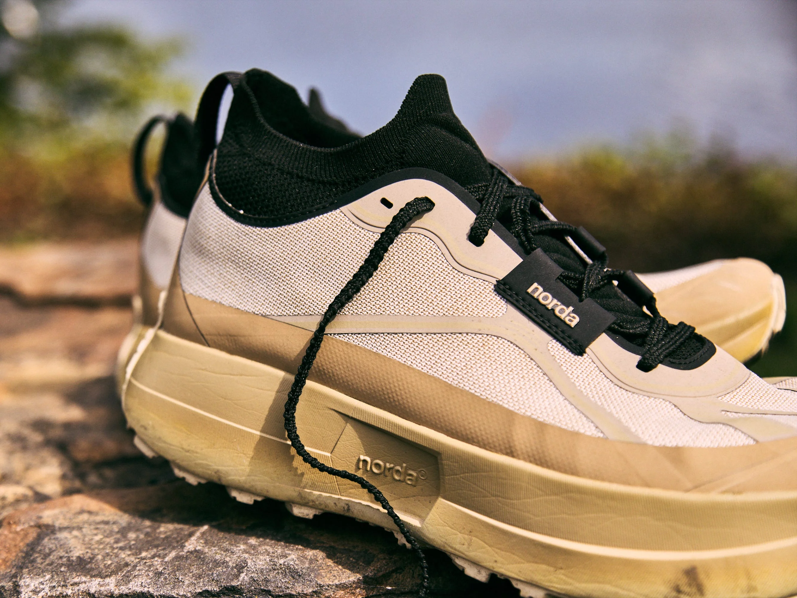 Close-up of a pair of norda 055 running shoes with a black and beige design resting on a rocky surface.