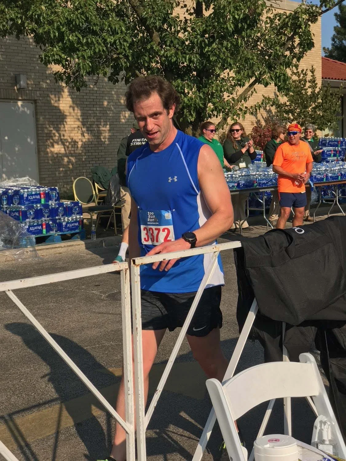 Runner crossing a finish line at an outdoor event, wearing a blue tank top and number 3872, with spectators in the background.