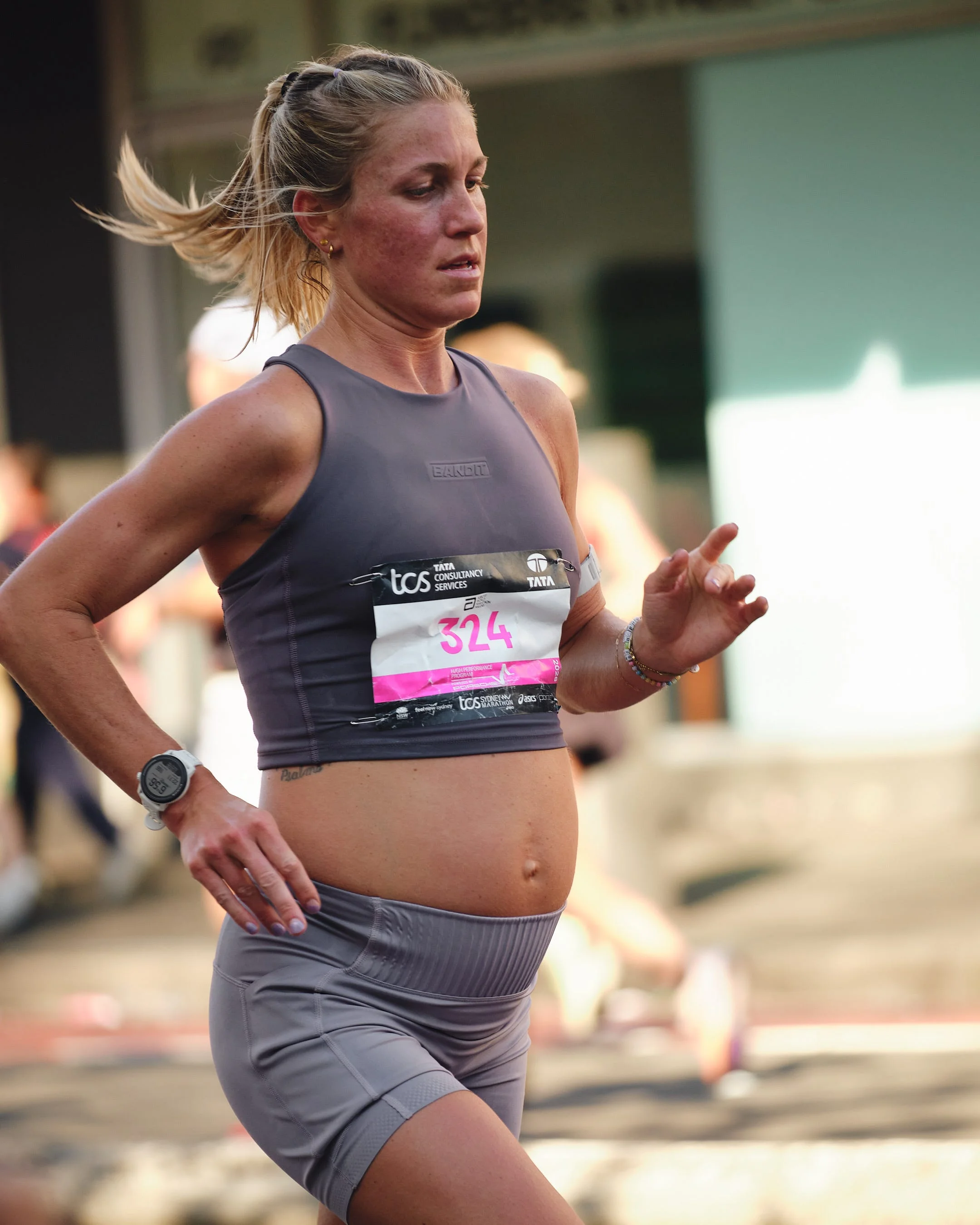 A pregnant woman running in a race, wearing a gray athletic outfit and a race number on her chest.