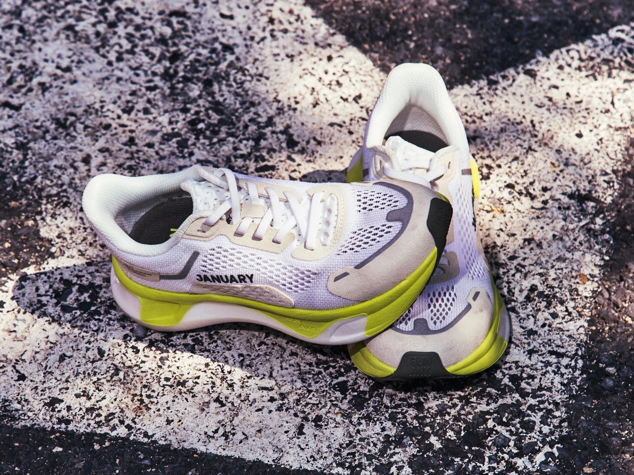 Sneakers with a light gray and yellow design resting on a painted arrow on asphalt.