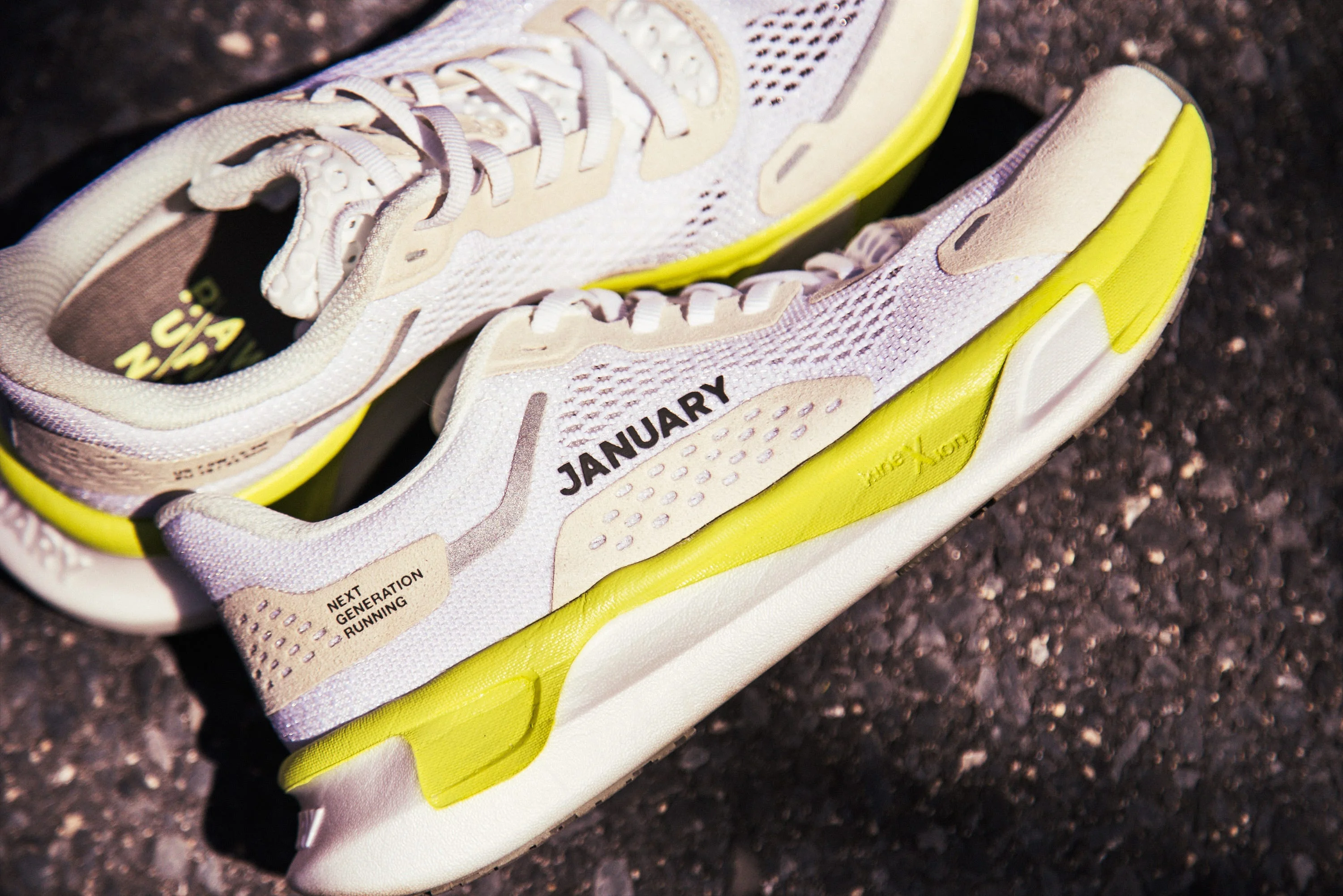 White and yellow running shoes with text "JANAURY" and "NEXT GENERATION RUNNING" on the side.