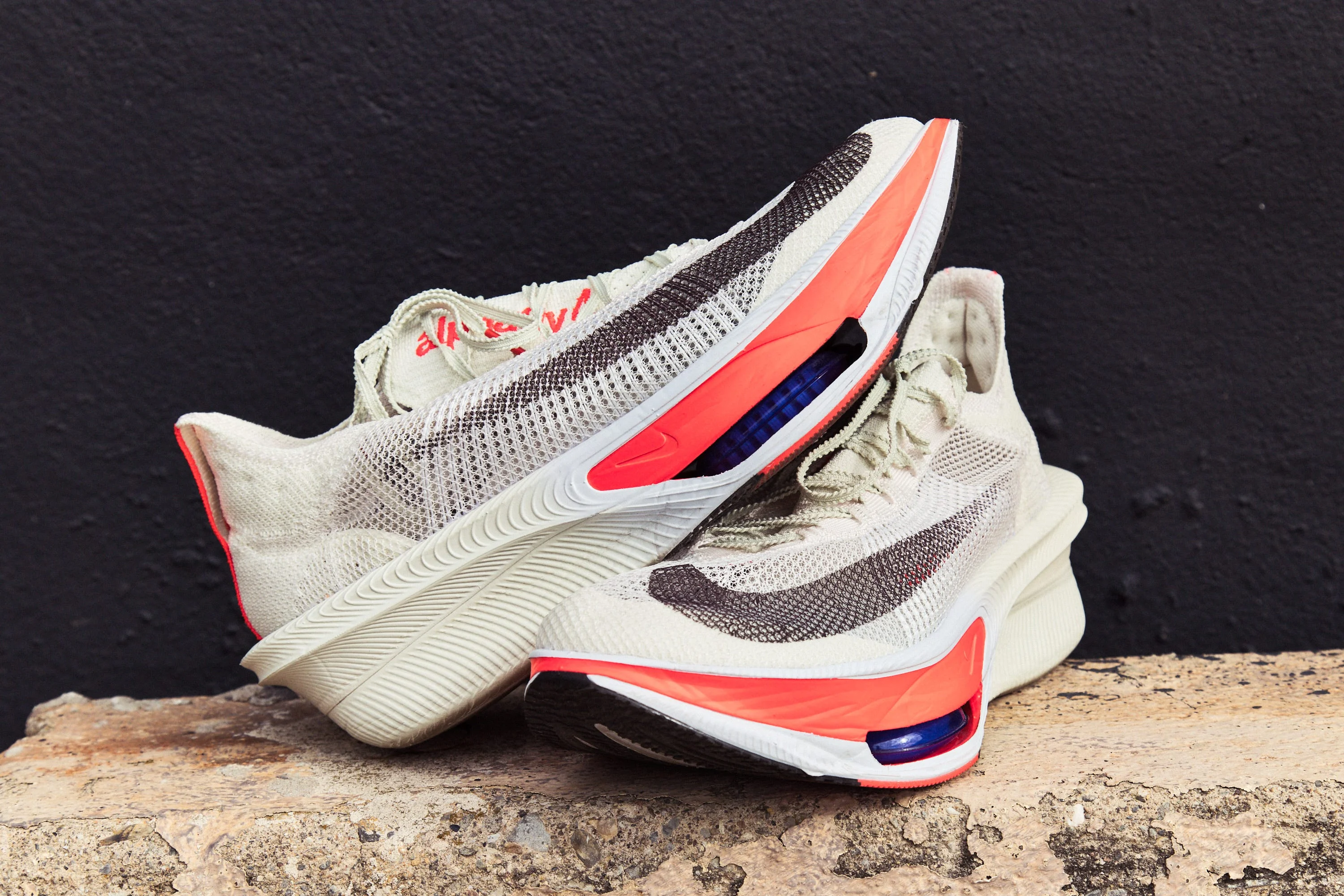 Lightweight athletic shoes with grey and red accents resting on a textured surface against a dark background.