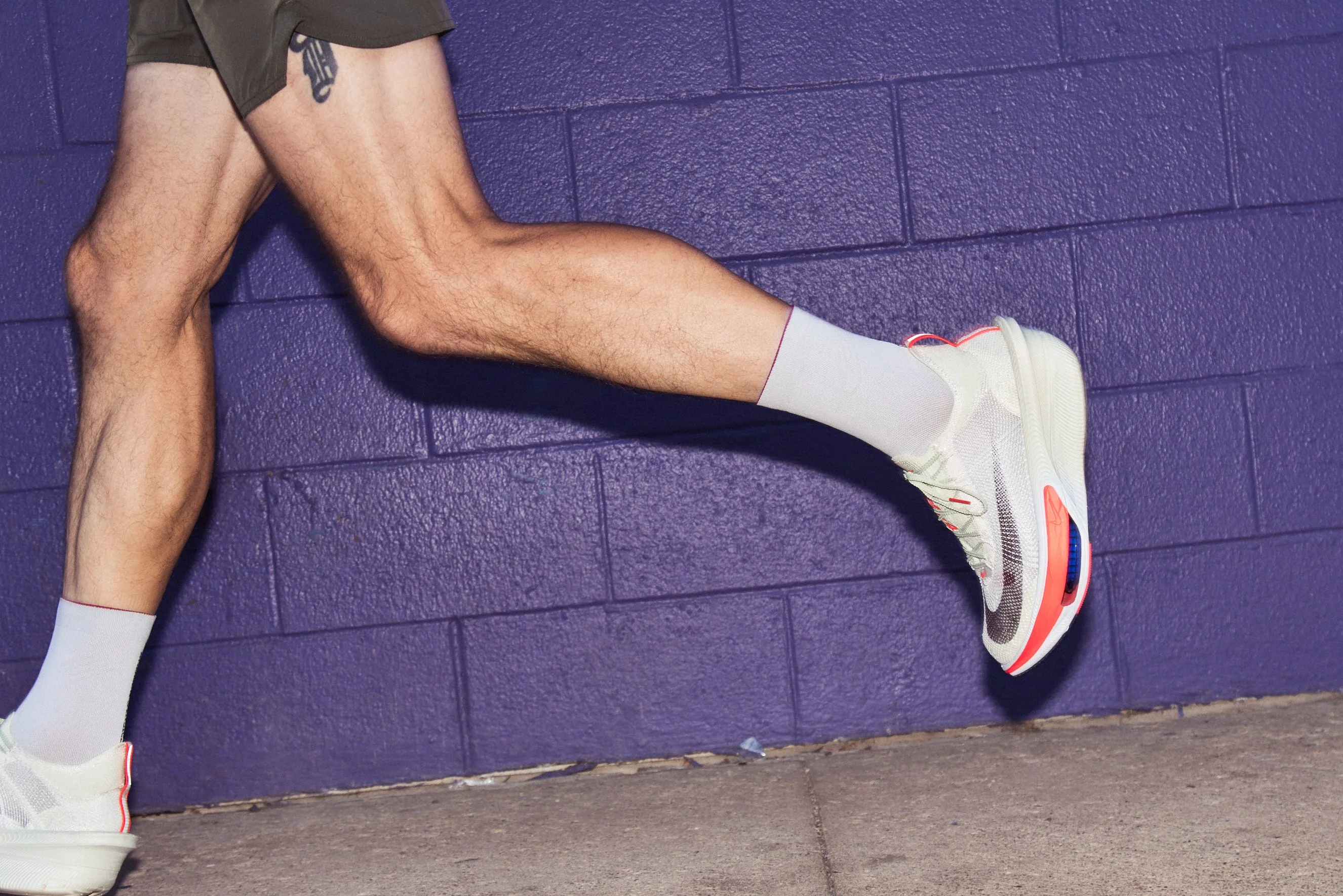 A runner showcasing athletic shoes against a purple wall.
