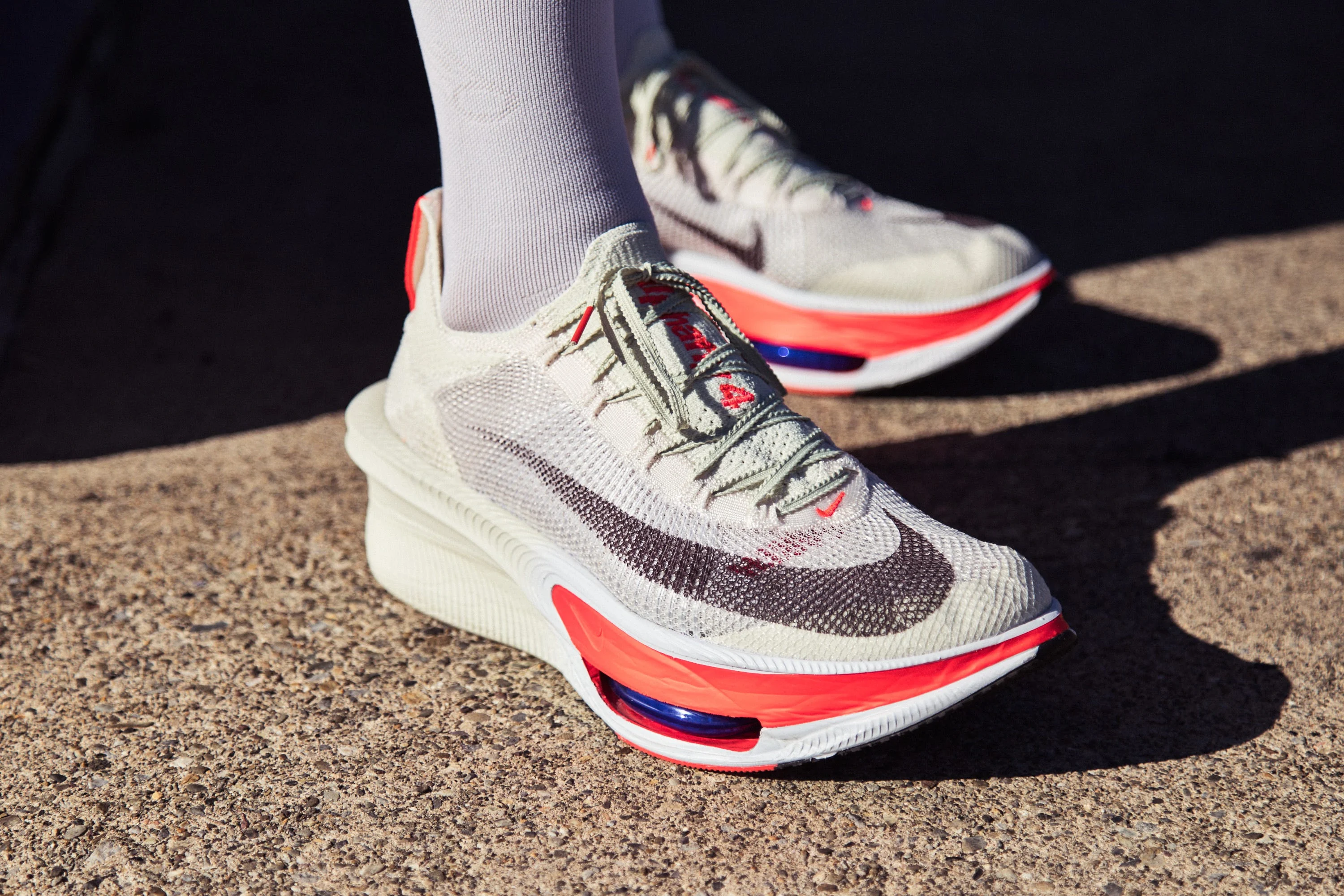 Modern athletic shoes with a grey and red design, featuring a prominent logo and unique sole structure.