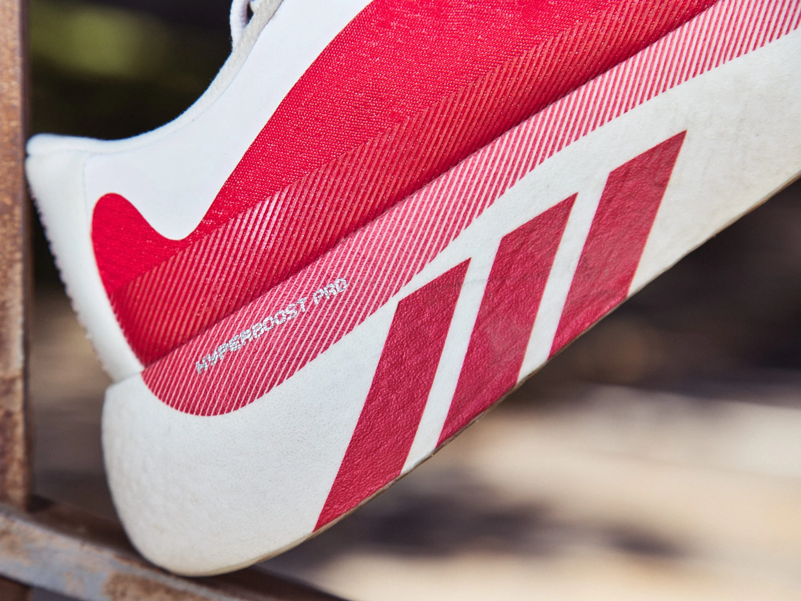 Red and white sneaker hanging on a metal railing, featuring a textured design and brand logo on the side.