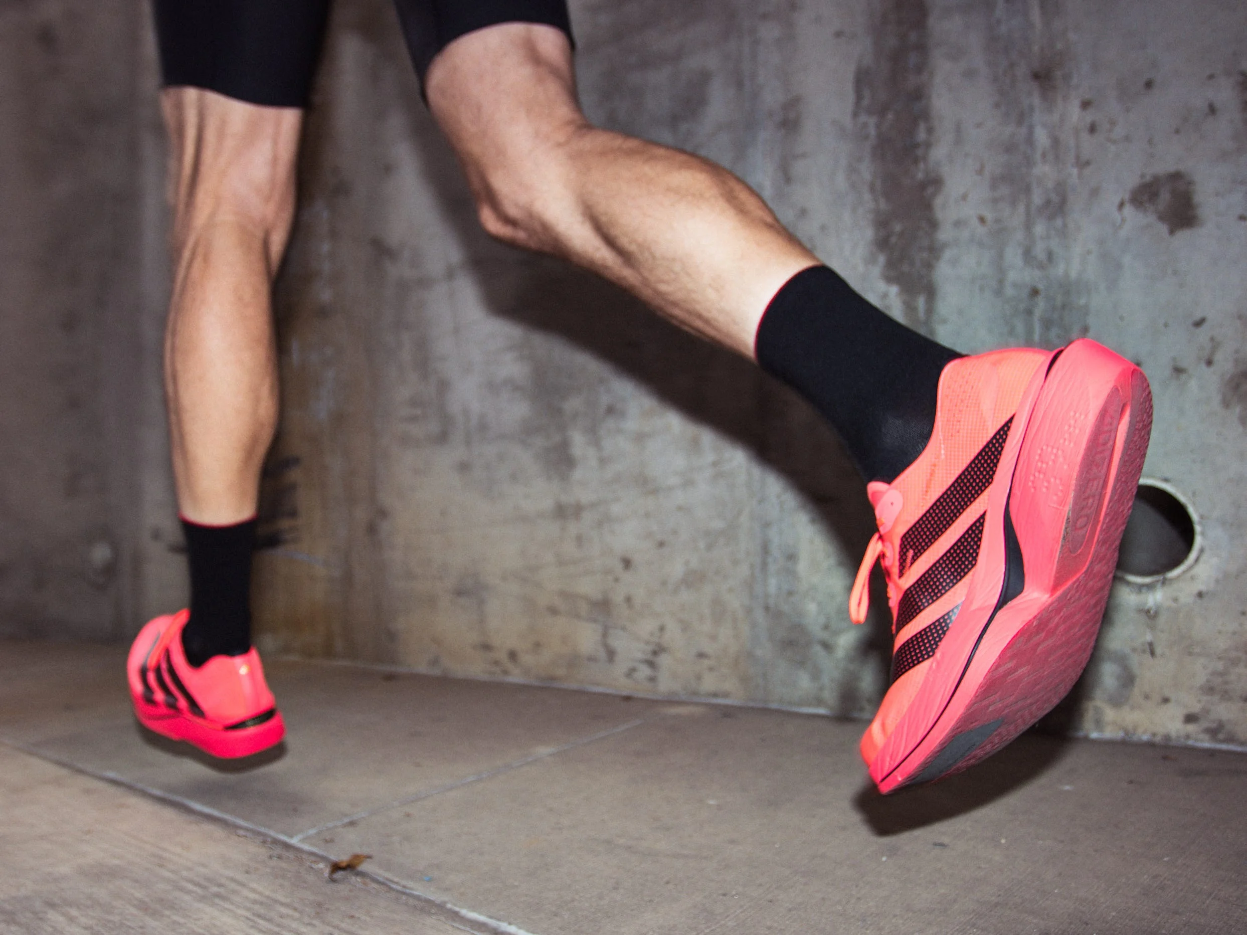 Close-up of a runner's foot wearing Adizero Adios Pro 5 shoes and black socks on a concrete surface.