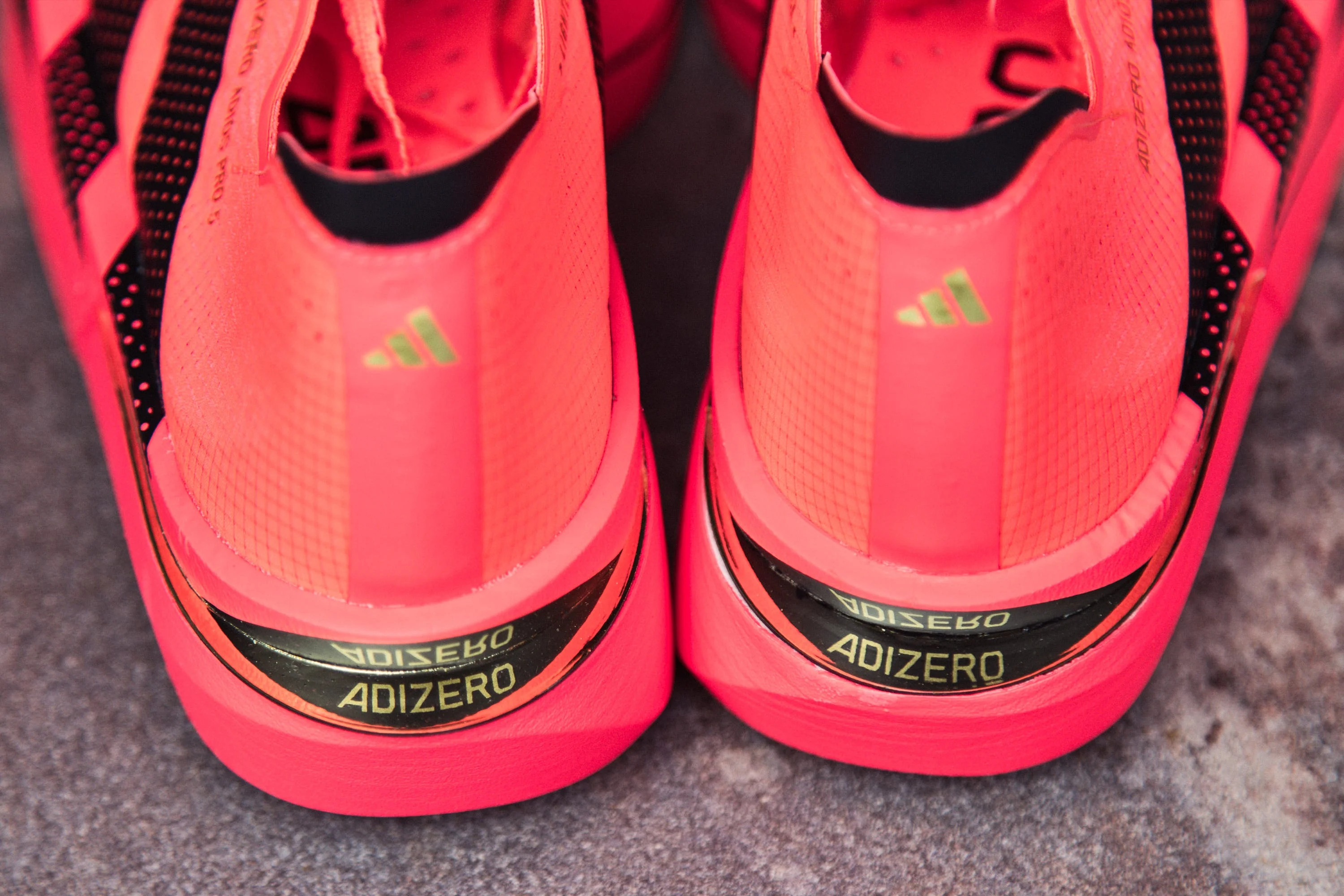 Bright pink Adidas Adizero shoes with black accents, showing the back view and distinctive branding.
