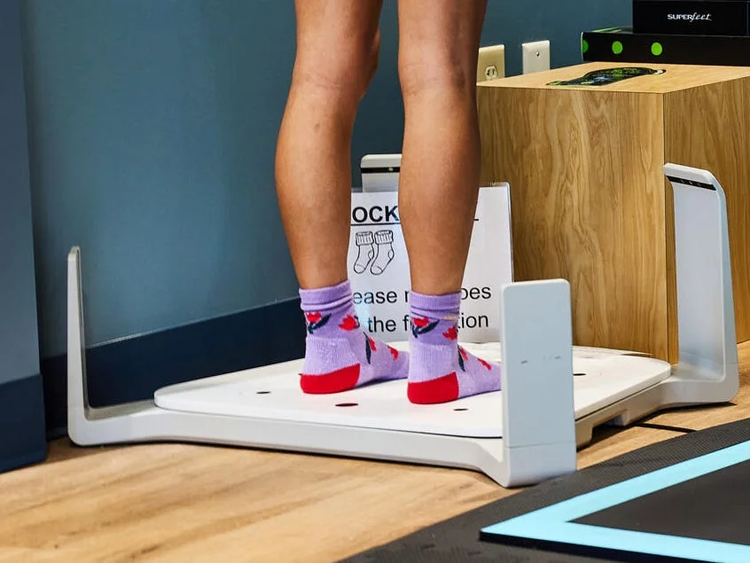 A person stands on a weighing device in a fitness center, surrounded by exercise mats and equipment.