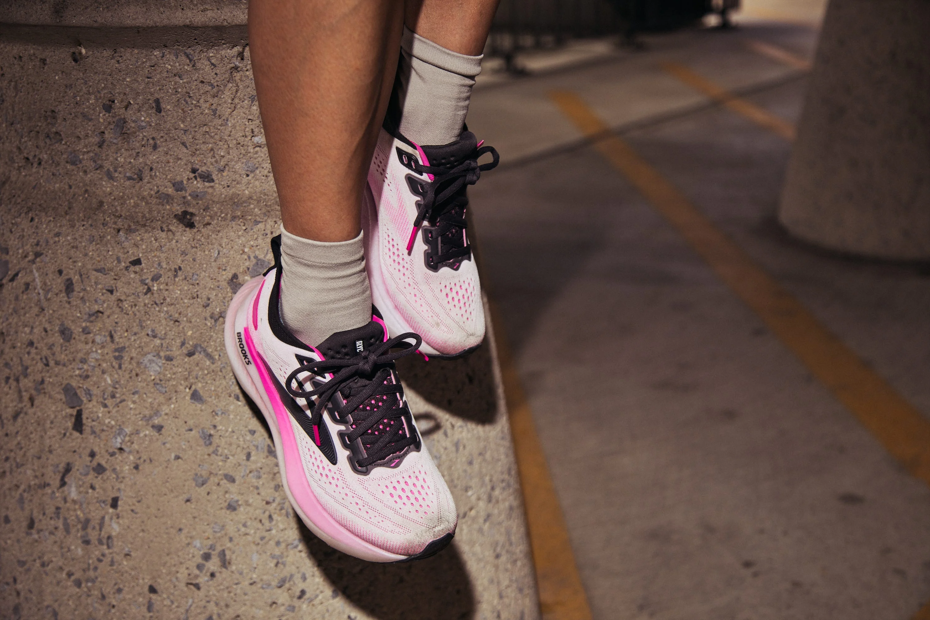 Pink and white running shoes on feet, resting against a concrete surface.