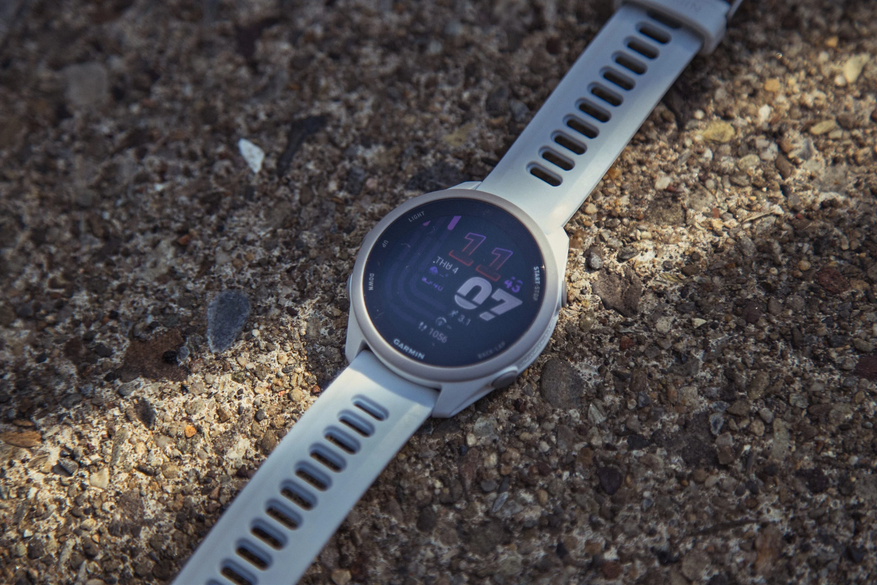 Smartwatch with white strap on textured surface displaying time and date.