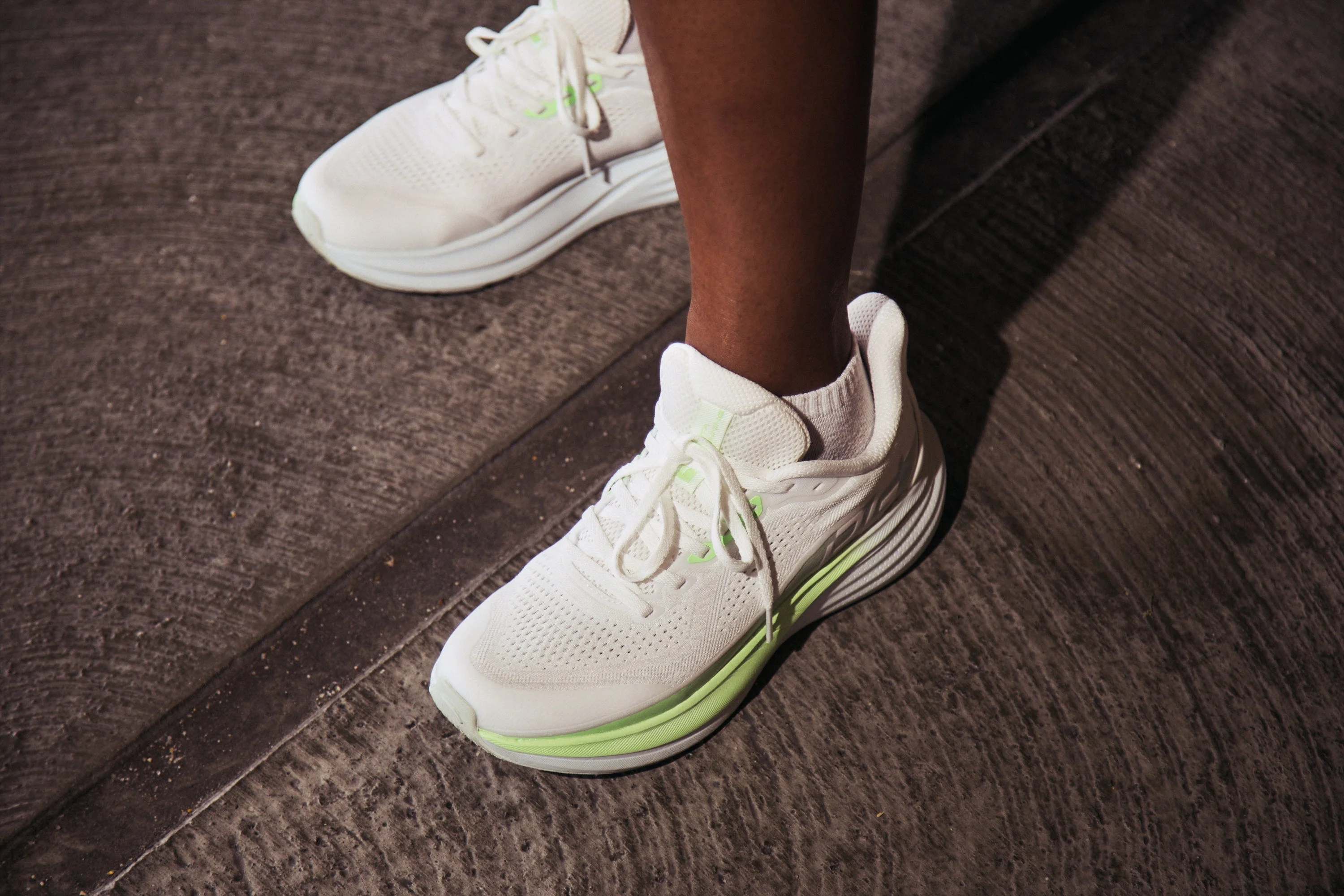 Person wearing white running shoes with green accents on concrete.